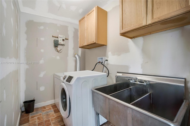 clothes washing area with cabinet space, baseboards, washer and clothes dryer, stone finish floor, and a sink