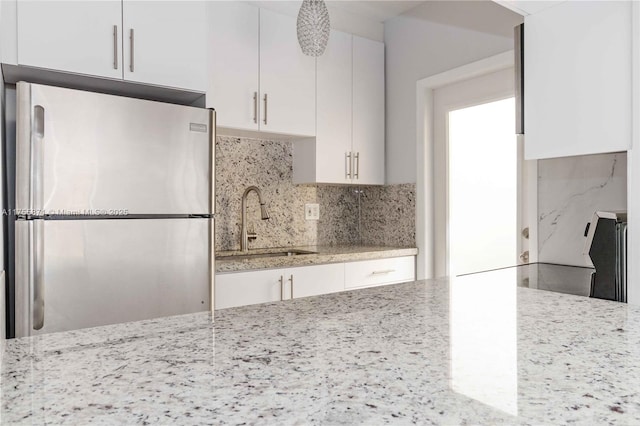 kitchen with light stone counters, tasteful backsplash, freestanding refrigerator, and white cabinets