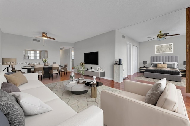 living room with a ceiling fan, light wood-type flooring, visible vents, and a textured ceiling