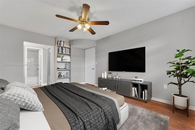 bedroom with baseboards, ceiling fan, wood finished floors, ensuite bathroom, and a textured ceiling