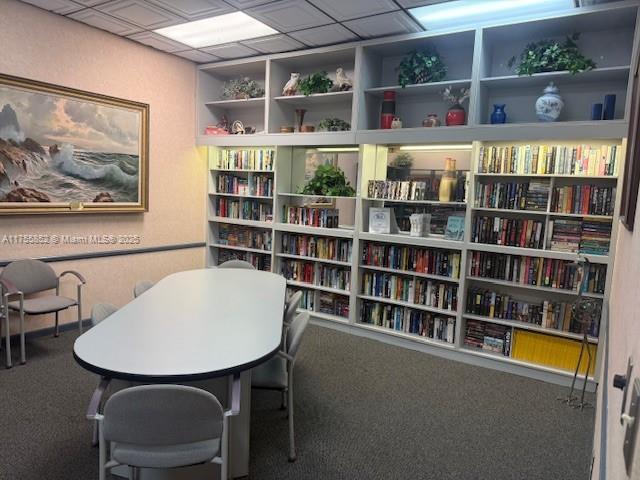 office area with carpet floors, built in shelves, a drop ceiling, and wall of books