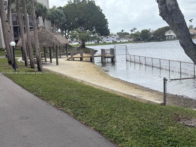 dock area with a water view, fence, and a lawn