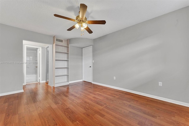 unfurnished bedroom with baseboards, a ceiling fan, wood finished floors, ensuite bathroom, and a textured ceiling