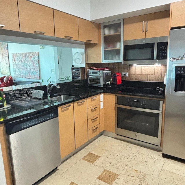 kitchen with stainless steel appliances, a sink, decorative backsplash, dark stone countertops, and glass insert cabinets