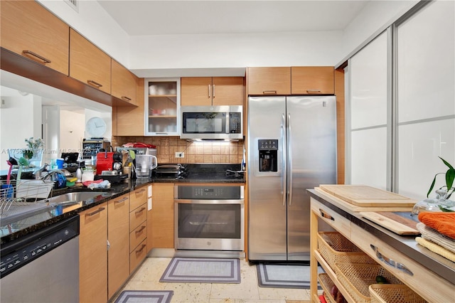 kitchen featuring tasteful backsplash, glass insert cabinets, dark stone countertops, stainless steel appliances, and a sink