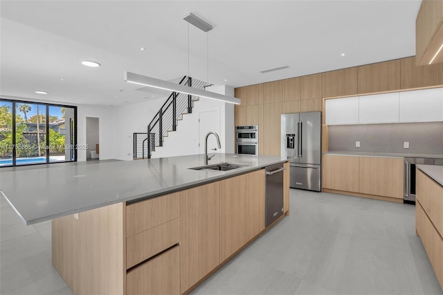 kitchen with a large island, modern cabinets, appliances with stainless steel finishes, light brown cabinetry, and a sink