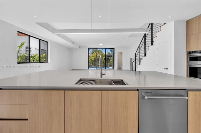 kitchen with modern cabinets, appliances with stainless steel finishes, open floor plan, light brown cabinets, and a sink