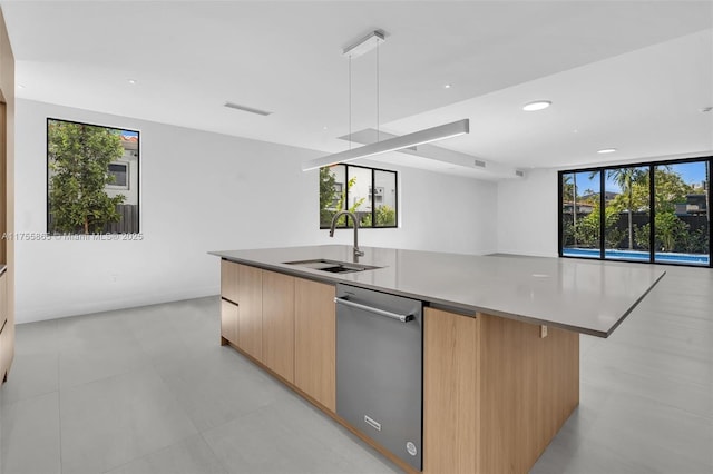 kitchen featuring light brown cabinets, a kitchen island with sink, a sink, stainless steel dishwasher, and modern cabinets