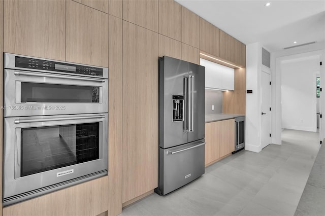 kitchen with stainless steel appliances, light countertops, light brown cabinets, modern cabinets, and beverage cooler