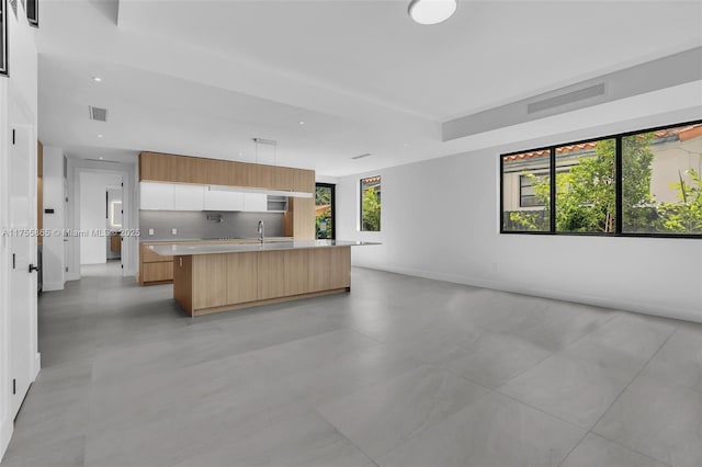 kitchen with a center island with sink, light countertops, visible vents, open floor plan, and modern cabinets