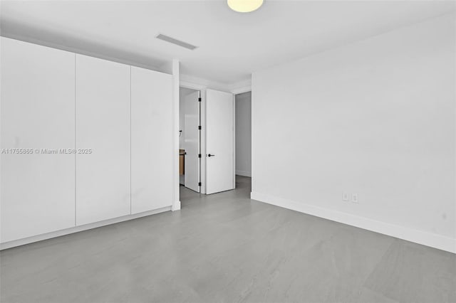 unfurnished bedroom with baseboards, concrete floors, visible vents, and a closet