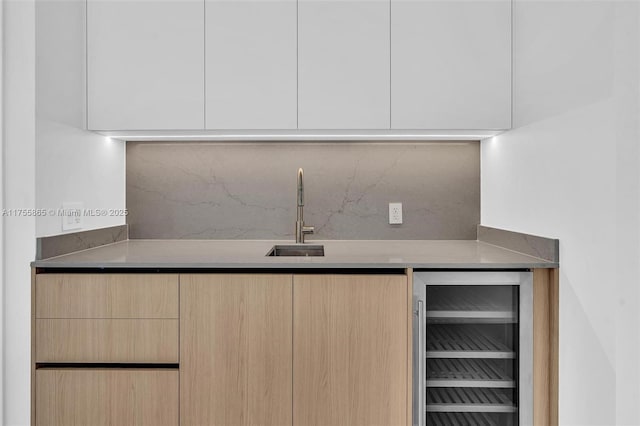 kitchen featuring wine cooler, backsplash, light brown cabinets, a sink, and modern cabinets