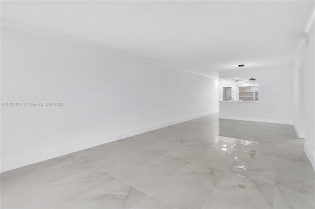 empty room featuring marble finish floor, a notable chandelier, crown molding, and baseboards