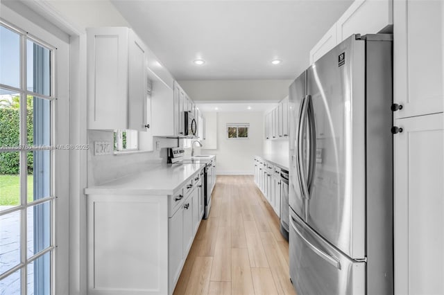 kitchen featuring appliances with stainless steel finishes, white cabinets, light countertops, and light wood-style floors