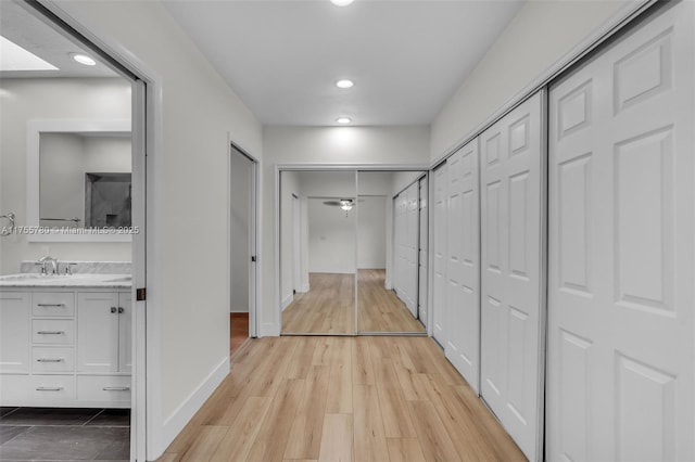 corridor featuring recessed lighting, baseboards, a sink, and light wood finished floors