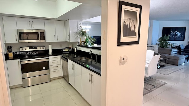 kitchen with dark countertops, light tile patterned floors, appliances with stainless steel finishes, and a sink