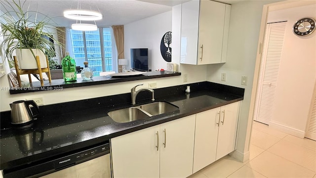 kitchen with dishwasher, dark stone countertops, white cabinetry, a sink, and light tile patterned flooring