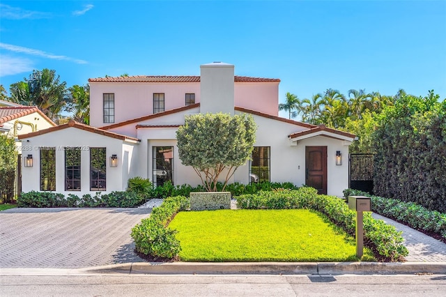 mediterranean / spanish home featuring a tile roof, a front lawn, and stucco siding