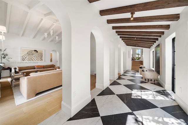 hallway with arched walkways, lofted ceiling with beams, and baseboards