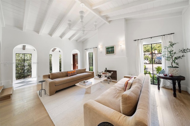 living room with light wood finished floors, plenty of natural light, arched walkways, and high vaulted ceiling