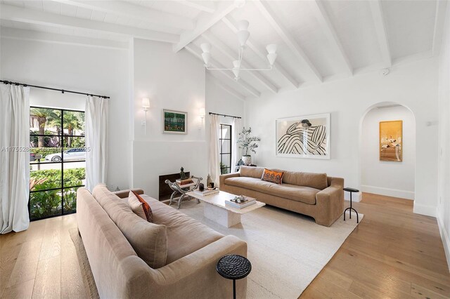 living room featuring arched walkways, high vaulted ceiling, baseboards, beam ceiling, and light wood finished floors