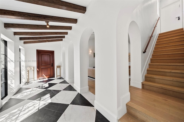 hall featuring baseboards, stairway, arched walkways, and beamed ceiling