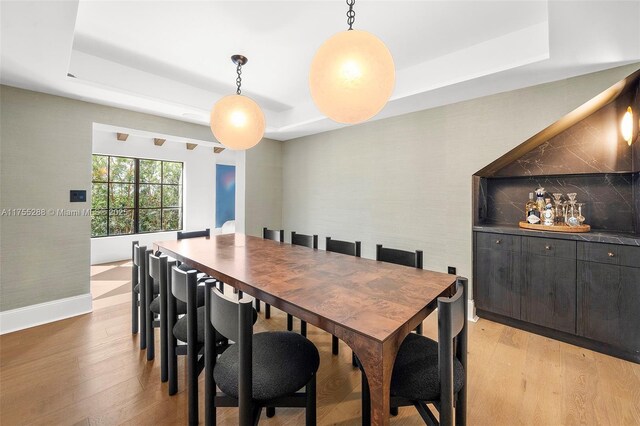 dining room with a tray ceiling, light wood-type flooring, and baseboards