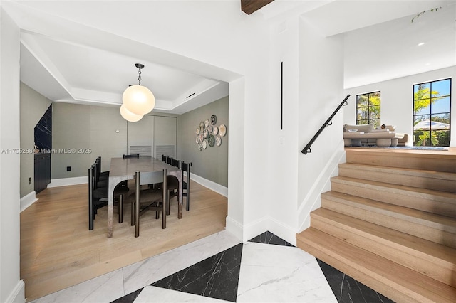 dining space featuring stairs, a tray ceiling, baseboards, and wood finished floors