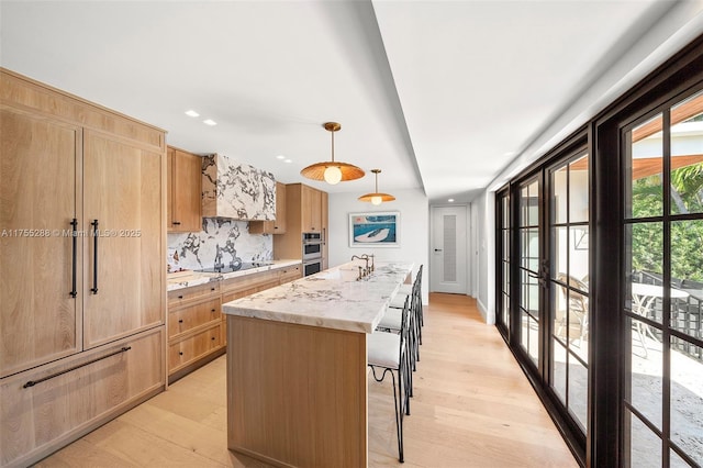 kitchen with black electric stovetop, light wood-style flooring, light brown cabinets, and a kitchen island with sink