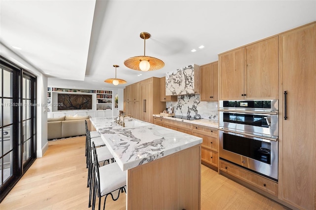 kitchen with double oven, light wood finished floors, an island with sink, and black electric stovetop