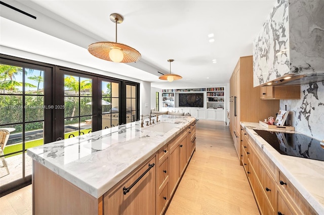 kitchen featuring pendant lighting, light wood-style floors, open floor plan, a sink, and light stone countertops