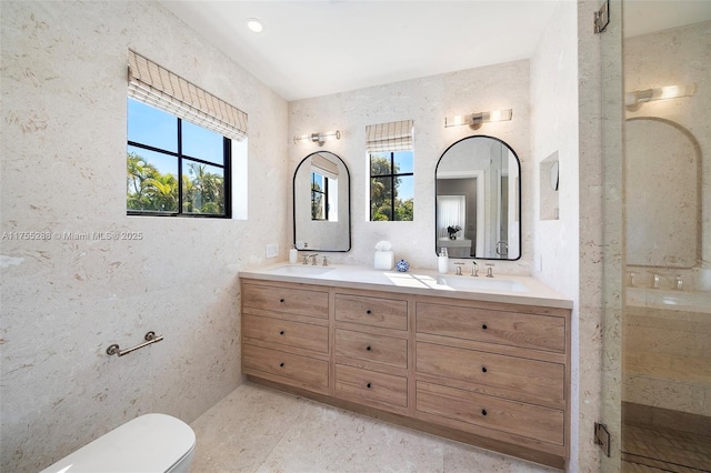 full bath featuring toilet, a stall shower, double vanity, and a sink