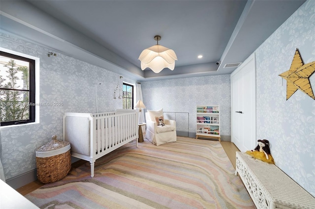 bedroom with baseboards, a tray ceiling, visible vents, and wallpapered walls