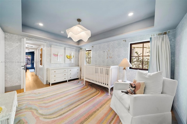 bedroom with wallpapered walls, a tray ceiling, and wood finished floors