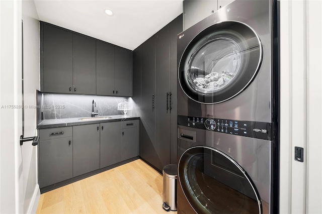 washroom with cabinet space, light wood-style floors, a sink, and stacked washer and clothes dryer