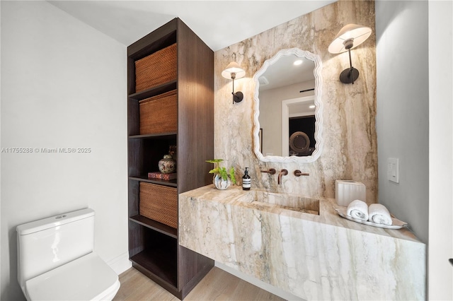 half bathroom with toilet, a sink, and wood finished floors