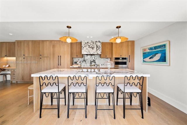 kitchen with a breakfast bar, stainless steel oven, light wood-style floors, decorative backsplash, and pendant lighting