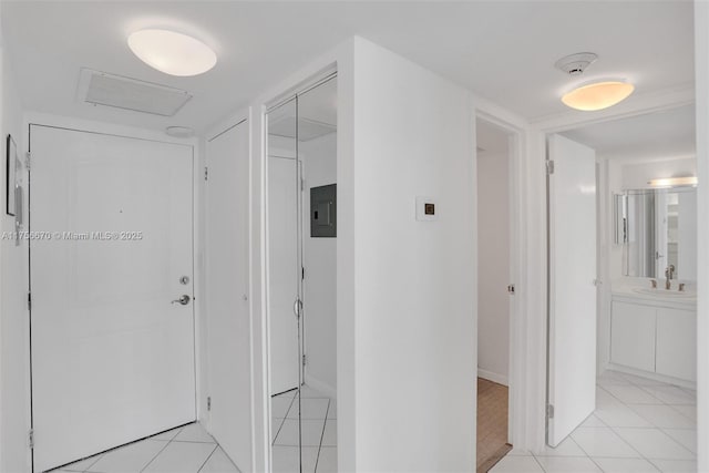 hall with light tile patterned floors, a sink, attic access, and electric panel