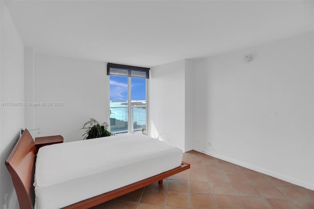 bedroom featuring expansive windows, light tile patterned flooring, and baseboards