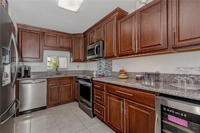 kitchen with light tile patterned floors, wine cooler, a sink, appliances with stainless steel finishes, and dark stone countertops