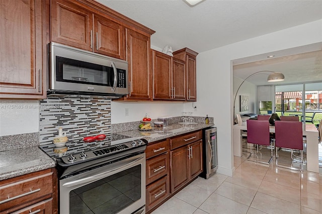 kitchen with light tile patterned floors, light stone counters, beverage cooler, stainless steel appliances, and backsplash