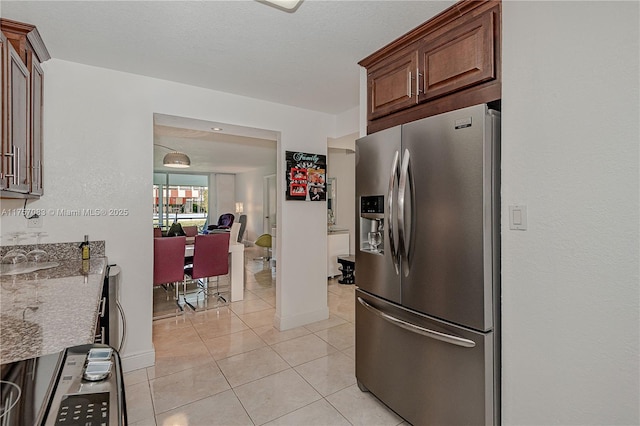 kitchen featuring stone countertops, stainless steel fridge, baseboards, and light tile patterned floors