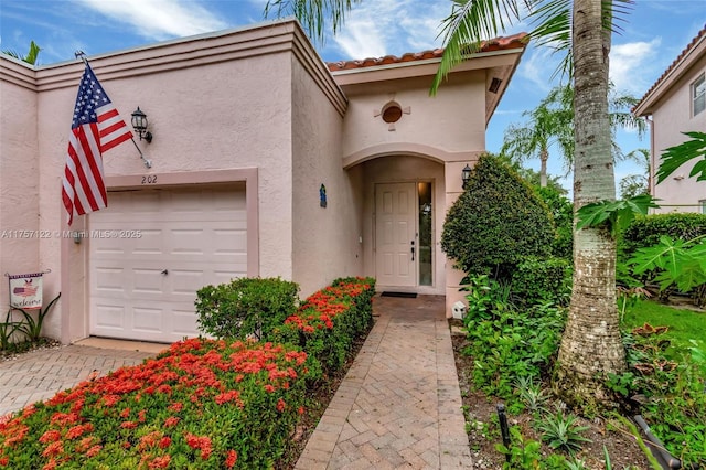 doorway to property with an attached garage, a tile roof, and stucco siding