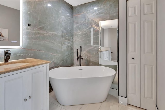 bathroom featuring a closet, a soaking tub, tile patterned flooring, vanity, and tile walls