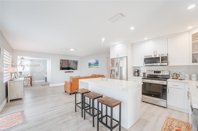 kitchen with stainless steel appliances, a kitchen island, visible vents, decorative backsplash, and a kitchen bar