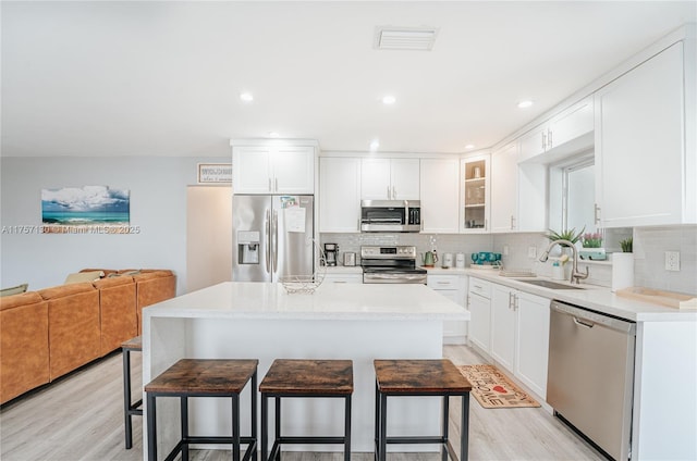 kitchen with a breakfast bar area, tasteful backsplash, appliances with stainless steel finishes, light wood-style floors, and a sink