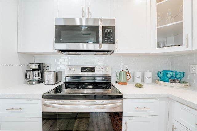 kitchen with stainless steel appliances, decorative backsplash, glass insert cabinets, and white cabinets