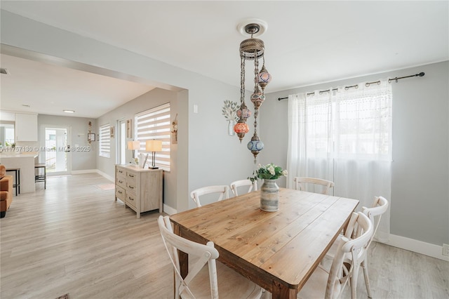 dining space featuring a fireplace, light wood-style flooring, and baseboards