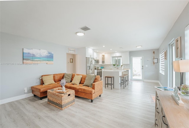 living room with light wood finished floors, baseboards, and visible vents