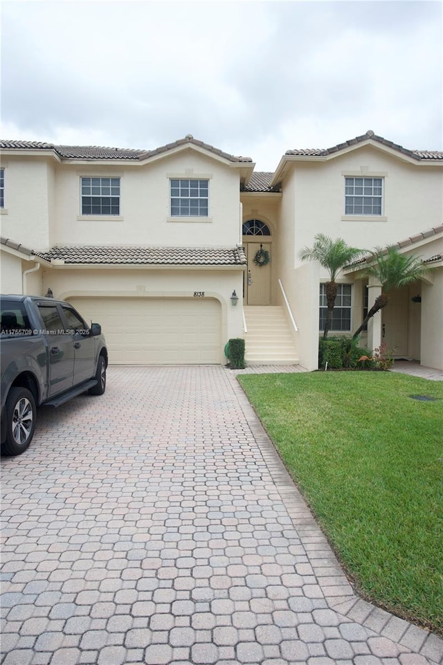 view of front facade with decorative driveway, a tile roof, stucco siding, an attached garage, and a front lawn